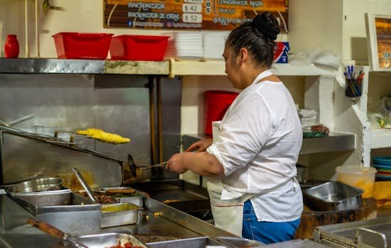 Woman in apron cooking traditional dishes in a busy restaurant kitchen.